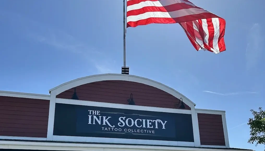 Storefront of The Ink Society on a sunny afternoon with large American Flag waving