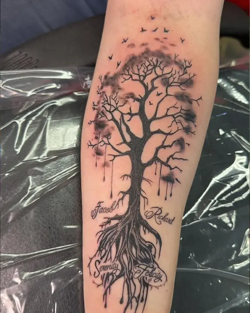Detailed black and grey gothic dead tree tattoo with roots, smoky clouds, and the names Jacob, Richard, Serenity, and Felicity written among the roots on the forearm.