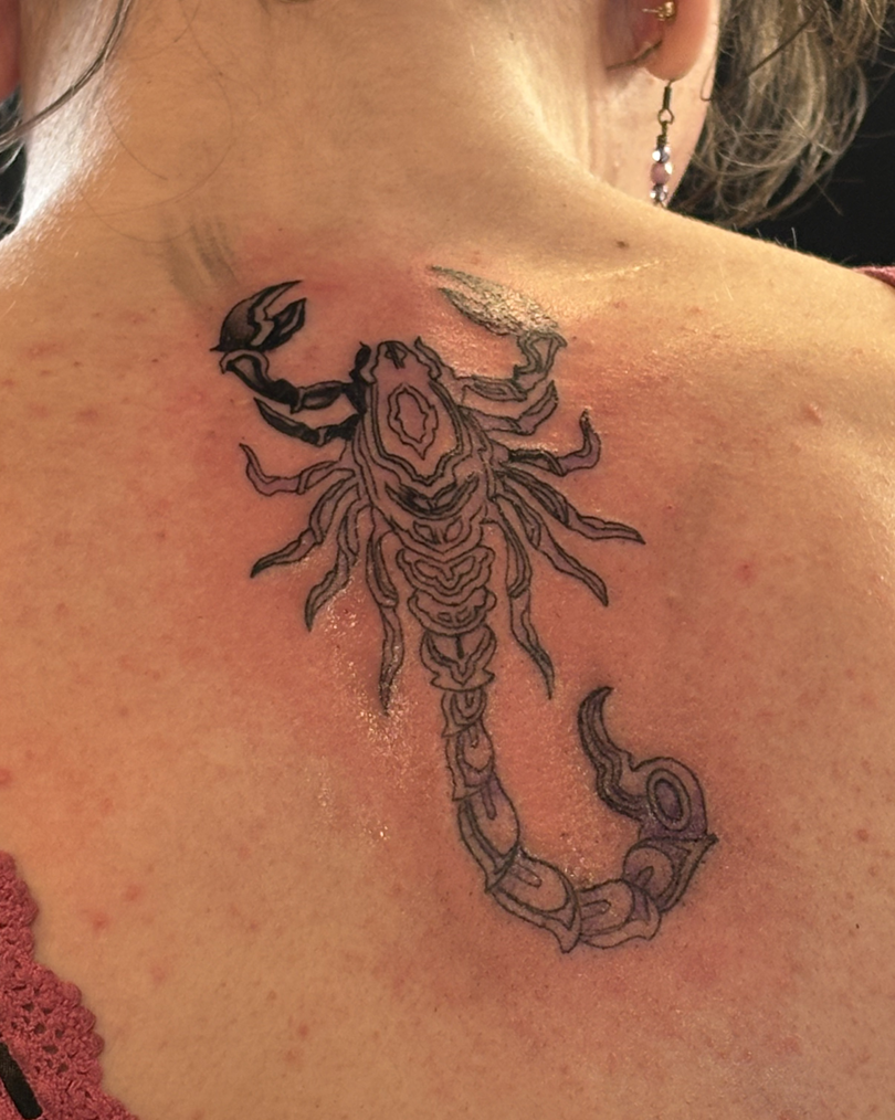 Detailed black outline scorpion tattoo placed on the upper back/shoulder blade of a client, featuring abstract line work within the body segments.