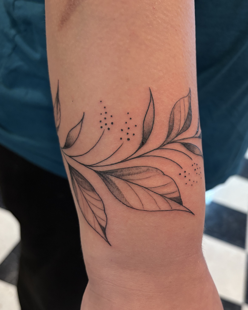 Close-up of a minimalist fine line black and grey botanical leaf and vine tattoo that wraps around the inner forearm.