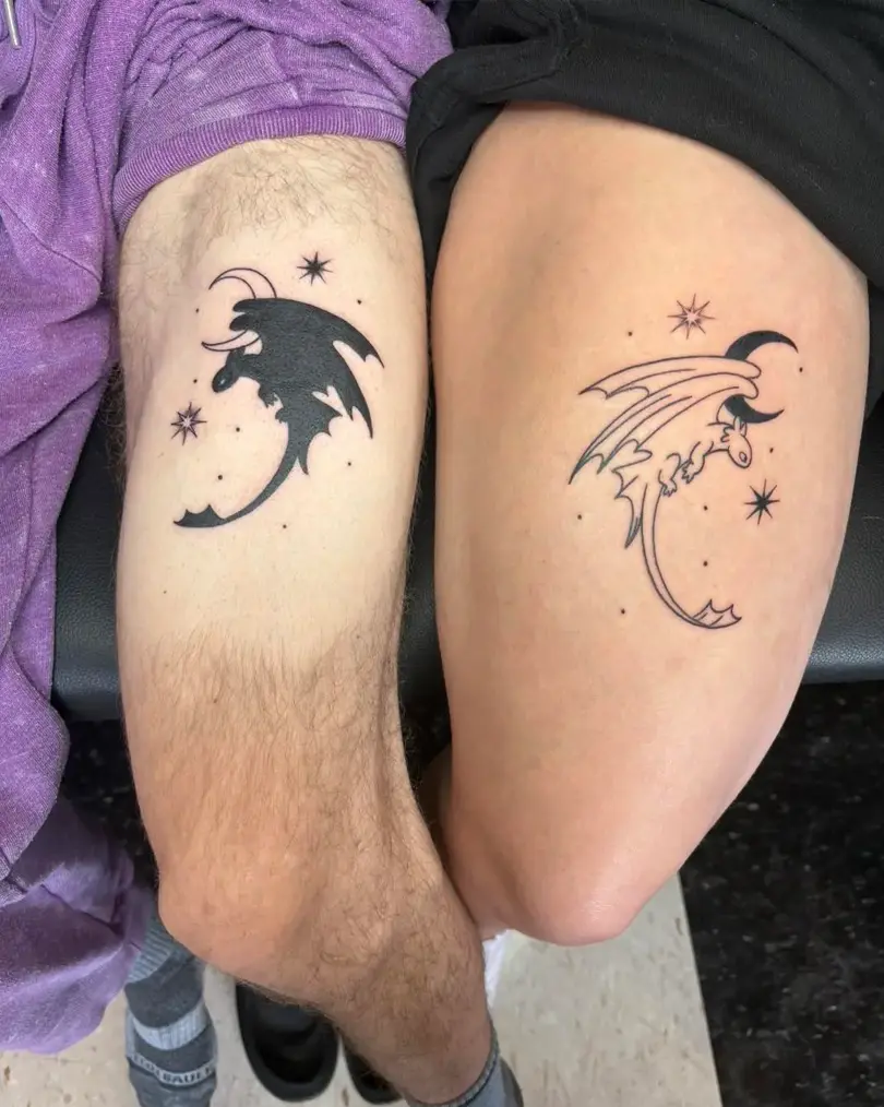 Matching couple's blackwork tattoos on the thigh of a small stylized dragon, moon, and stars; one is a solid black silhouette and the other is a fine line outline.